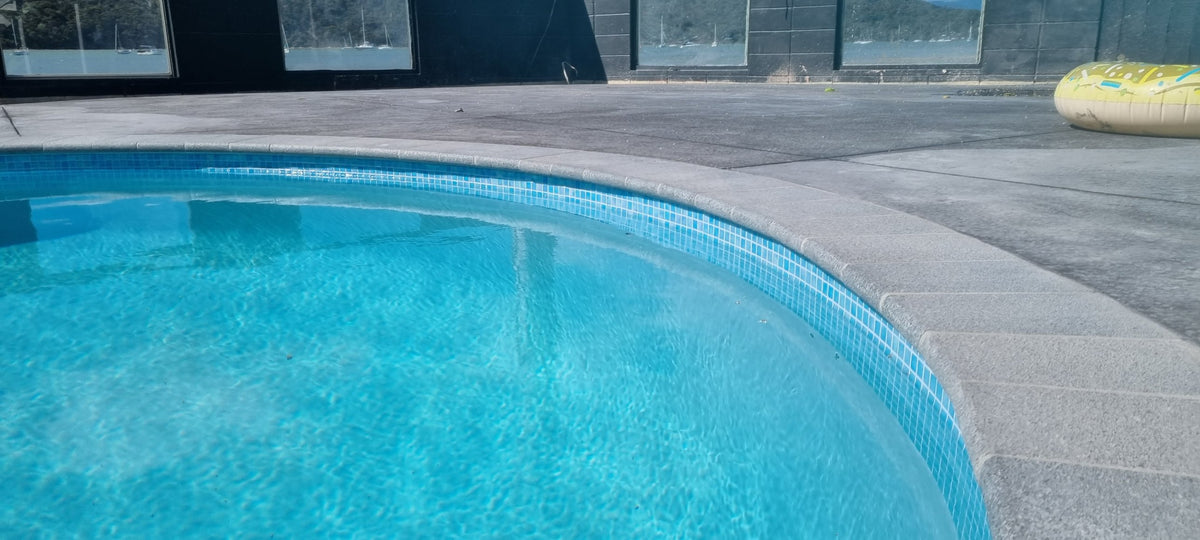 Flamed grey granite bullnose coping following the curve of a mosaic-lined pool