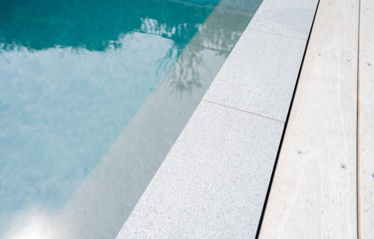 Close-up of flamed grey granite square edge coping beside hardwood decking