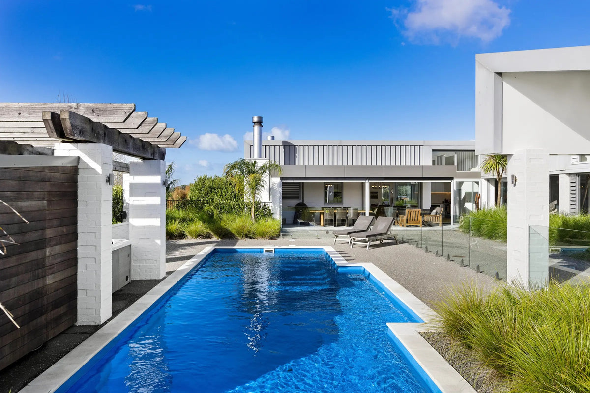 Light sandstone coping edging a blue pool beside a modern home